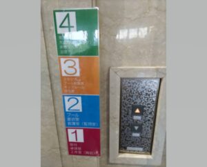 エレベーターのボタンとその隣に１階から４階までの案内が書かれている写真