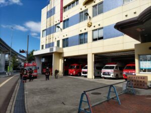 摂津市役所の隣の消防署に救急車や消防車があり、消防士さんが消防車の隣で話し合っている写真